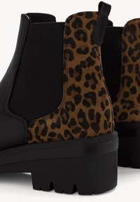 Bottes cheville en cuir noir et daim imprimé léopard marron avec semelles épaisses noires et panneaux latéraux élastiques.