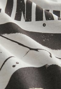 Cotton T-shirt, white with a black graphic print. Features bold text and abstract shapes, demonstrating a soft, smooth texture.