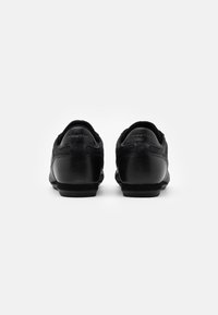Schwarze Lederschuhe mit glatter Textur, runder Zehenform und niedrigem Gummisohlenprofil. Die Rückansicht zeigt ein minimales Branding an der Ferse.