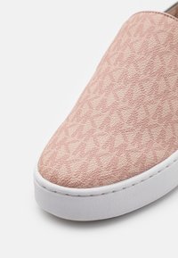 Gros plan sur l'avant d'une basket rose texturée avec un motif géométrique et une semelle en caoutchouc blanche sur fond blanc.