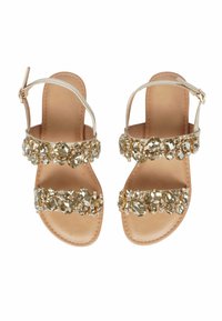 Sandali piatti dorati con due cinturini decorati da cristalli e una cinghia alla caviglia. La soletta è color tan, con una texture liscia e un design minimalista.