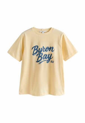 Light yellow short-sleeve T-shirt with blue cursive "Byron Bay AU" text printed on the front, crew neckline, and relaxed fit.