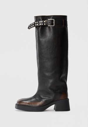 Stivale alto in pelle nera con tacco a blocco e una cinghia con borchie e una fibbia argentata attorno alla parte superiore del gambale.
