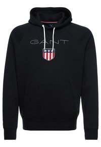 Zwarte hoodie met capuchon, voorzien van het GANT-logo in grijs en een rechthoekig geborduurd embleem met rode, witte en blauwe sterren en strepen. Voorzak.