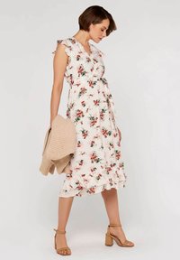 Floral midi dress with ruffled sleeves, light pink background, red and green patterns. Paired with a beige knitted cardigan and tan heeled sandals.