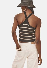 Top corto acanalado en marrón oscuro con rayas beige, con un diseño de espalda cruzada. Combinado con pantalones cargo de color claro.