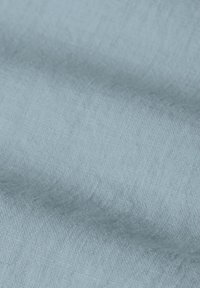 Tissu bleu clair avec une surface douce et texturée, présentant de légers plis qui créent des ombres délicates.