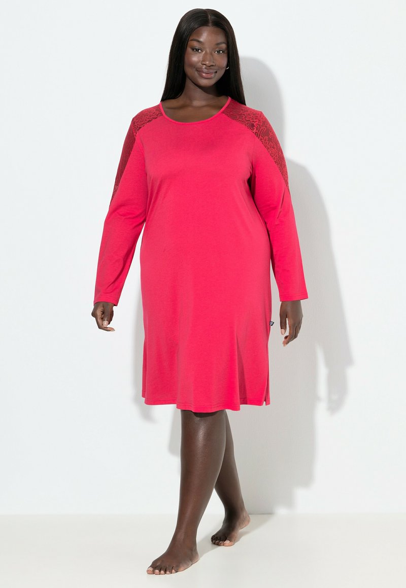 Camisón rosa de mangas largas con acentos de encaje en los hombros, fabricado en un tejido suave, con corte a la altura de la rodilla y aberturas laterales para facilitar el movimiento.