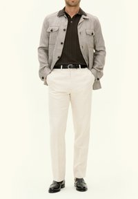 Men's outfit featuring a light plaid jacket, dark textured polo, and cream-colored trousers, complemented by black loafers.