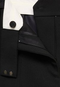 Black tailored trousers featuring a white button closure, zip pocket, and sleek fabric. Includes metal hardware accents on the waistband.