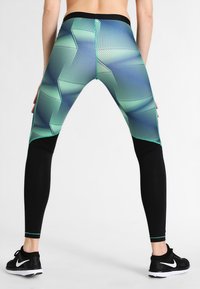 Leggings à motifs noirs et verts avec un design géométrique, dotées d'une taille haute et de panneaux noirs contrastants sur le bas des jambes.