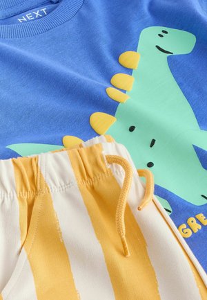 Blaues Baumwoll-T-Shirt mit einem grünen Dinosaurier-Grafik und gelben Akzenten; kombiniert mit gestreiften Shorts in Creme und Gelb mit elastischem Bund.