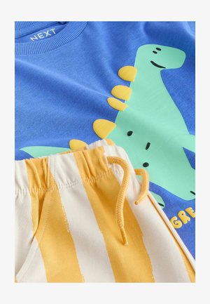 Blå bomullströja med en grön dinosauriegraphic med gula detaljer; tillsammans med randiga krämfärgade och gula shorts med elastiskt midjeband.
