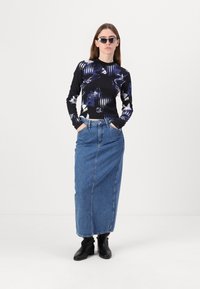 Svart langermet topp med abstrakte blå og hvite mønstre, kombinert med en høy midje denim maxiskjørt og svarte ankelstøvler.