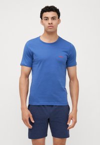 T-shirt en coton bleu à manches courtes et encolure arrondie. Présente un petit logo rouge sur la poitrine. Associée à un short bleu foncé.
