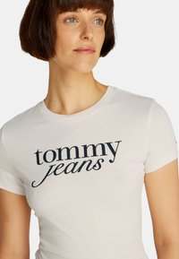 Maglietta in cotone bianco con logo "tommy jeans" blu navy, colletto tondo e maniche corte con un design aderente.