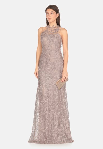 Abito da sera lungo beige elegante con ricami floreali, corpino aderente, scollatura a halter e texture a strati. La modella tiene una piccola pochette luccicante.