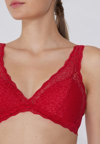 Bralette de encaje rojo con un escote en V profundo, patrones florales y tirantes anchos de encaje. Textura suave y cierre de gancho en la parte trasera.