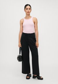 Top sem mangas rosa claro, calças largas pretas, sapatos de plataforma pretos de dedo aberto e uma pequena mala preta com um design estruturado.
