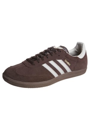 Zapatilla Adidas Samba de ante marrón con rayas blancas, forro interior blanco, cordones marrones y texto "SAMBA" en dorado en el lateral.