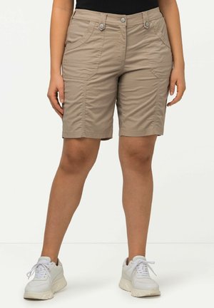 Shorts cargo beiges avec poches avant, deux fermetures à bouton et détails de couture visibles. Portés avec des baskets blanches.