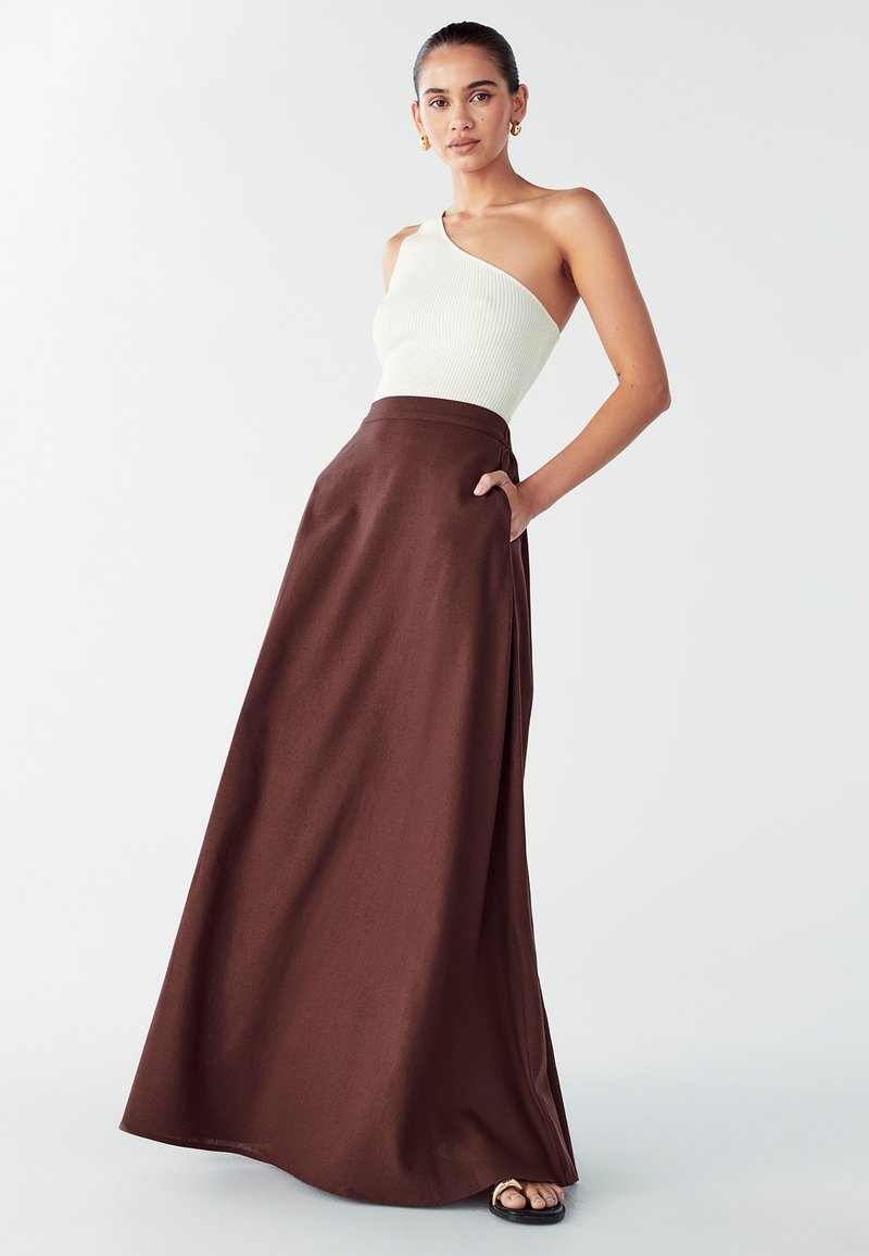 Asymmetrisch wit geribbeld topje gecombineerd met een lange, donkerbruine rok met zakken en een gladde textuur. Elegante silhouet.