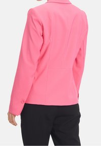 Figurpassad rosa blazer, mjukt tyg, strukturerade axlar, enfingerknappar och detaljering på baksidan. Bärs tillsammans med svarta byxor.