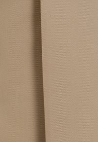 Tissu beige texturé avec un léger éclat et un motif de tissage en diagonale, montrant deux plis superposés le long du bord.