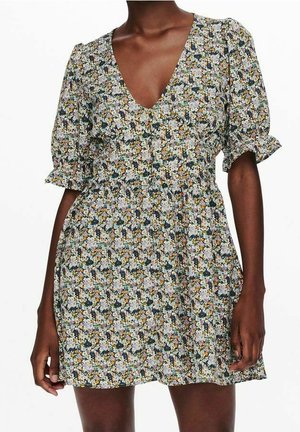 Femme portant une courte robe fleurie avec des manches bouffantes, un décolleté en V profond et une taille froncée dans un motif multicolore.