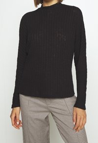 Czarny sweter prążkowany z wysokim kołnierzem i długimi rękawami, wykonany z fakturowanej tkaniny, zestawiony z spodniami w kratkę.