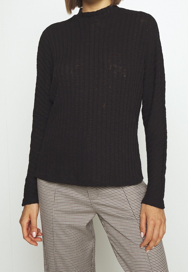 Czarny sweter prążkowany z wysokim kołnierzem i długimi rękawami, wykonany z fakturowanej tkaniny, zestawiony z spodniami w kratkę.