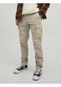 Beige cargobyxor i bomull med flera klafffickor, lös passform och förstärkningar i sömmarna, tillsammans med svarta högklackade sneakers.