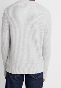 Grauer Strickpullover mit gerippter Textur, runder Ausschnitt und weiten Bündchen. Die Rückseite zeigt ein dezentes V-förmiges Nahtdetail.