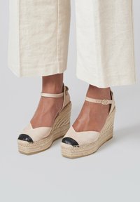 Beige espadrille wedge sandalen met een zwarte neus, enkelsluiting en een geweven jute zool; zachte suede textuur, afgeronde neusdesign.