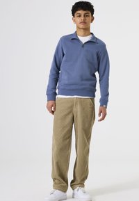 Sudadera azul con media cremallera, combinada con pantalones de pana color beige y zapatillas blancas. Presenta puños acanalados y bolsillos laterales.