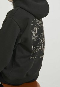 Svart hoodie i bomullsblandning, med vita grafiska illustrationer på baksidan. Designen inkluderar text och handritade element.