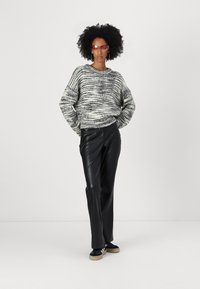Teksturert svart-hvitt genser med løs passform, kombinert med tettsittende bukser i svart kunstskinn. Modellen har på seg røde solbriller og svarte sneakers.