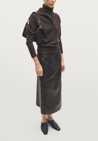 Maglione marrone a maglia grossa, design con collo alto; gonna midi in pelle marrone; scarpe in pelle nera con punta affusolata; piccola borsa nera.