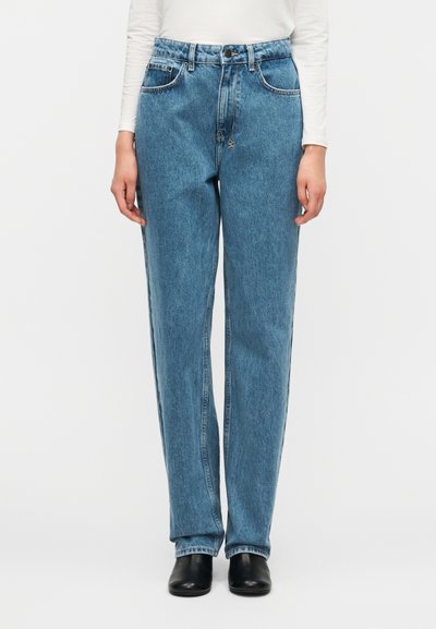 Τζιν παντελόνι από ανοιχτό μπλε denim με ίσια γραμμή, ψηλή μέση, πέντε τσέπες και εμφανείς ραφές. Συνδυάζεται με μαύρα παπούτσια.