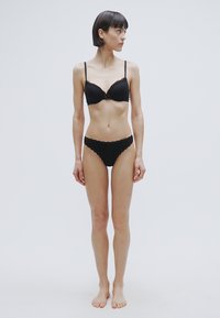 Ensemble de lingerie noire comprenant un soutien-gorge rembourré à bords festonnés et un bas bikini assorti, tous deux en tissu lisse et mat.