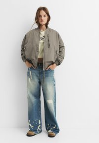 Világosszürke bomber dzseki, pamut keverékből, cipzáros elülső résszel és oldalsó zsebekkel. Zöld, cropped toppal és kopott, bő szabású kék farmernadrággal viselve.