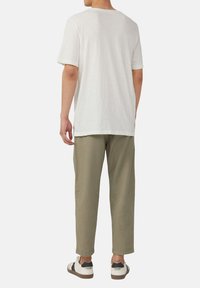 Witte kortey T-shirt van lichtgewicht stof, gecombineerd met olijfgroene, relaxte broek en zwart-witte sneakers.