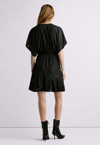 Robe courte noire à coupe décontractée, tissu texturé, manches mi-longues, ourlet à volants, portée avec des bottines noires.