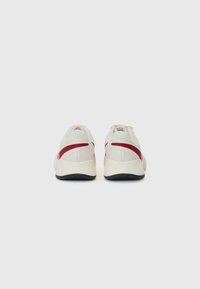 Sporty sneakers with a beige mesh upper, red accents, and a textured black rubber sole. Features a low-profile design and cushioned heel.