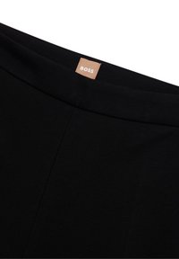 Mustapöytä, jossa on sileä, joustava kangas. Siinä on litteä vyötärö ja valkoinen "BOSS"-tunnus. Yksinkertainen muotoilu ilman kuvioita.