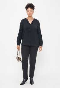 Mustapaitainen pitkähihaine paita V-mallisella kaula-aukolla yhdistettynä mustiin slim fit -housuihin. Asusteita ovat pieni eläinkuosilla varustettu käsilaukku ja mustat korot.