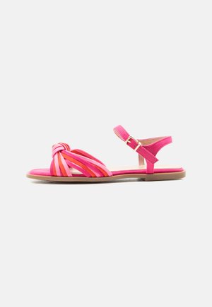 Flache pinke Sandale mit roten und pink verdrehten Frontriemen, Knöchelriemen mit goldener Schnalle und naturfarbener Sohle auf weißem Hintergrund.