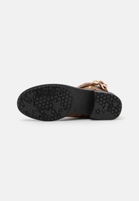 Suola in gomma nera con dettagli a stella e marchio; tomaia marrone con elementi metallici e cinghie; design piatto adatto per un look casual.