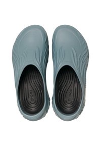 Hellblaue Slipper aus Gummi mit wellenförmiger Textur, abgerundeten Kanten und schwarzem Innenfutter, das ein wellenförmiges Muster aufweist.