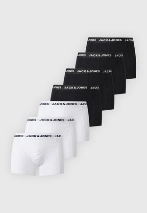 Hemdenloser Mann steht barfuß in schwarzen Jack & Jones Boxershorts vor einfachem hellem Hintergrund.